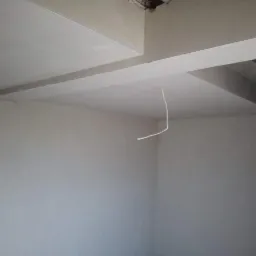 Wnętrze po nałożeniu gładzi, widoczny fragment wystającego kabla elektrycznego z sufitu. Świeżo wykończone ściany i sufit w odcieniach szarości.