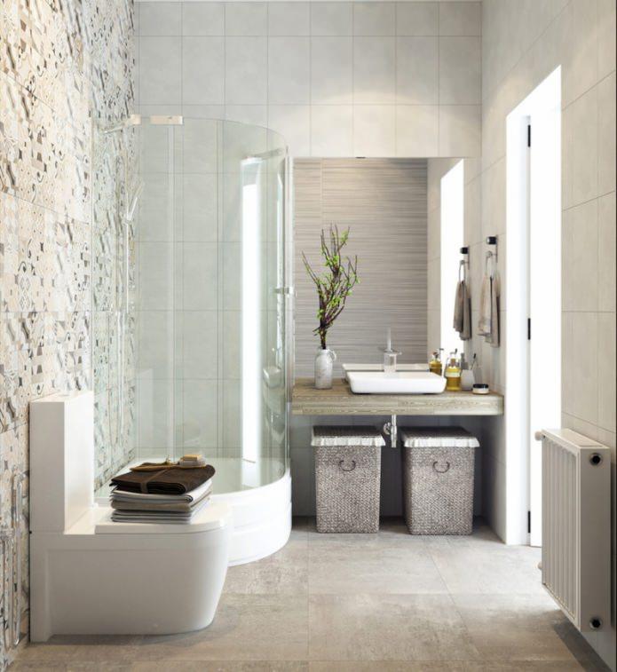 Jasna łazienka z kabiną prysznicową o zaokrąglonym kształcie, umywalką na drewnianym blacie, koszami z wikliny i toaletą z ułożonymi ręcznikami. Ściana wyłożona dekoracyjnymi płytkami.