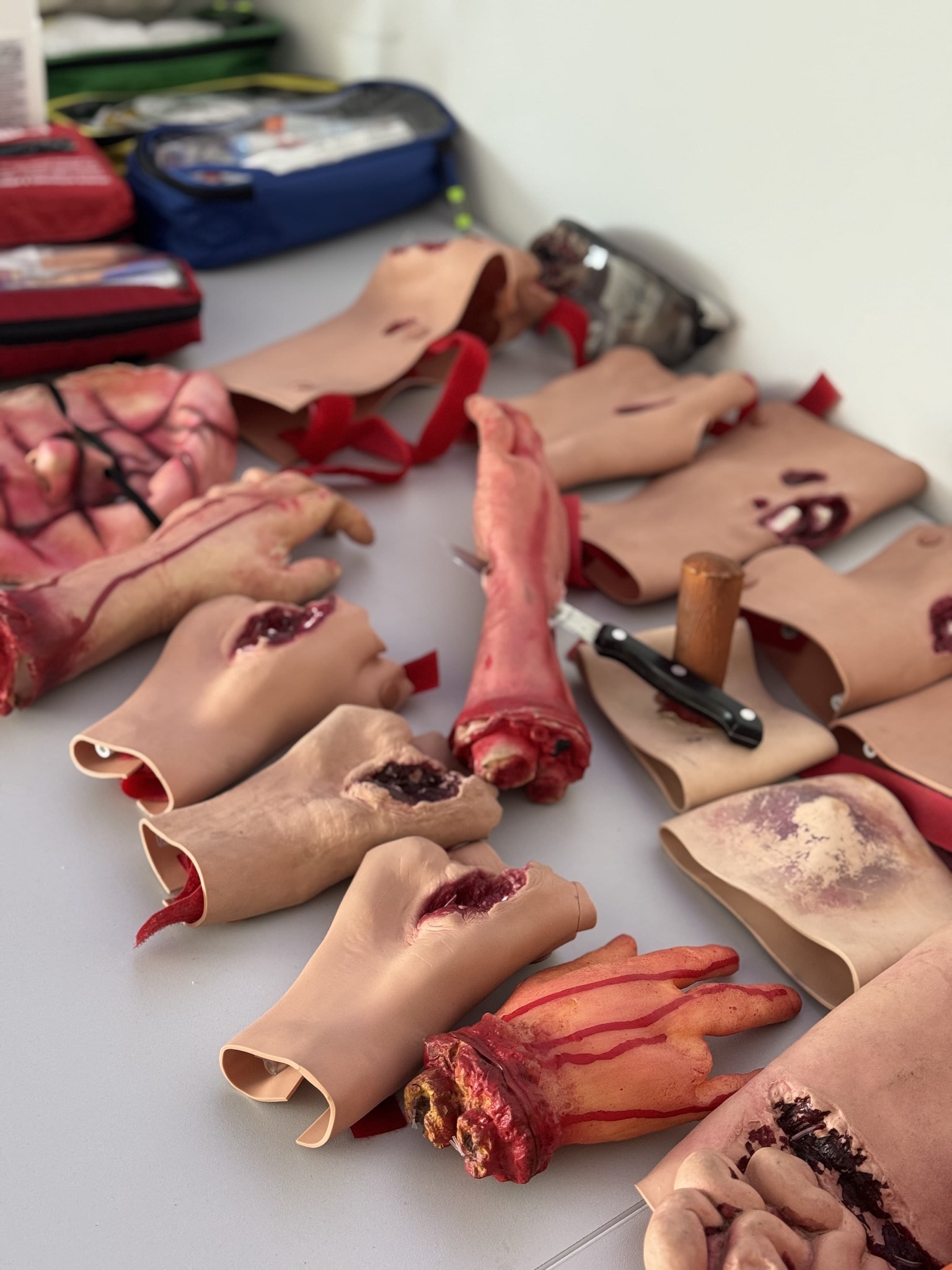 Manekiny rąk i nóg z symulowanymi ranami, nóż i apteczki. Sprzęt do ćwiczeń pierwszej pomocy na stole.