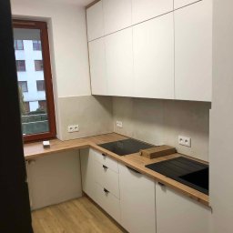 Master Furniture - Nowoczesna kuchnia z białymi szafkami i drewnianym blatem, widok na okno z widokiem na budynek mieszkalny, płyta indukcyjna i zlew w kolorze czarnym.