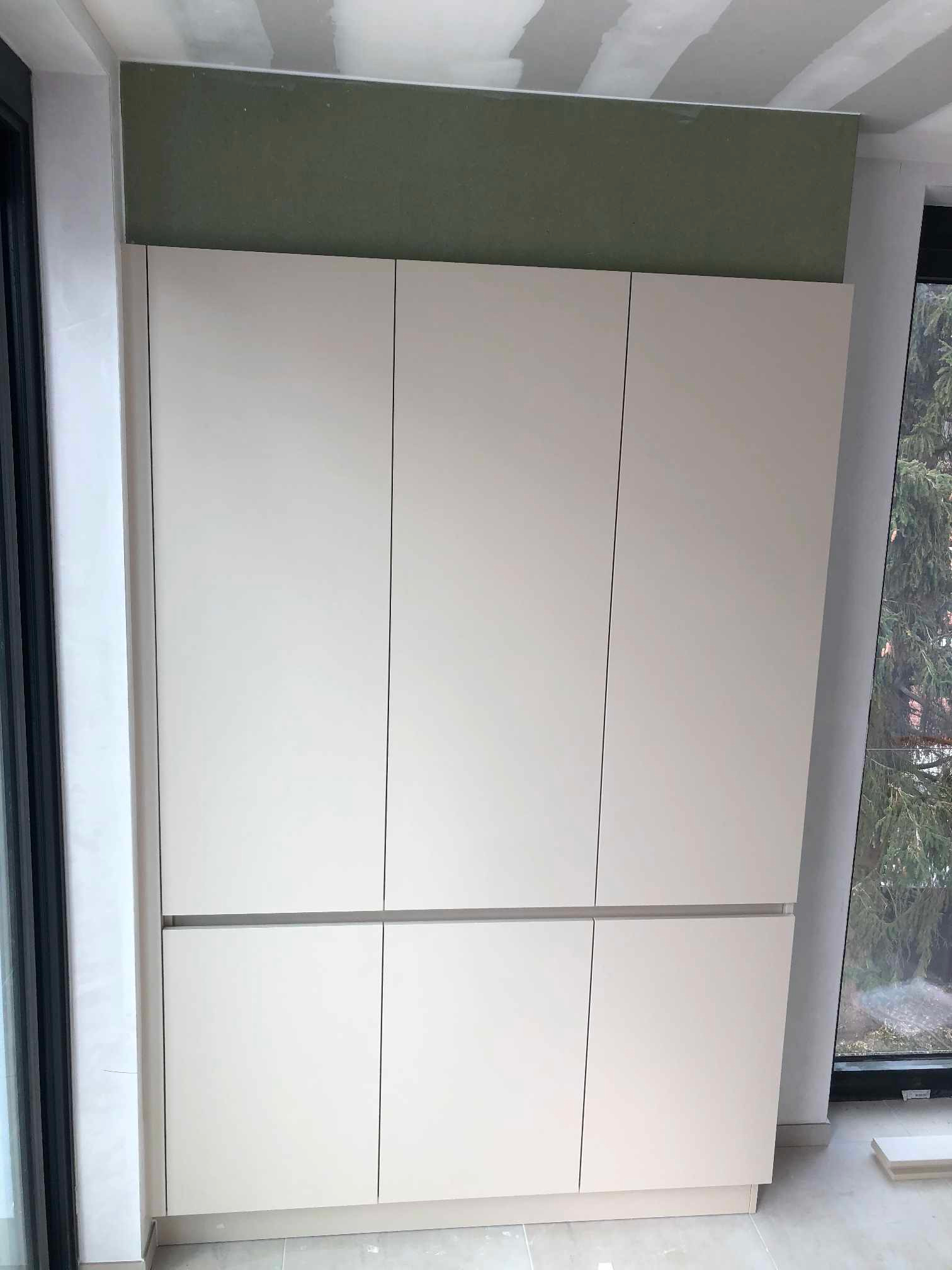 Jasna, sześciodrzwiowa szafa zamontowana pod sufitem w nowym budynku, widok z boku na tle okna i zielonego drzewa.