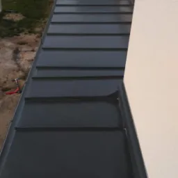 Nowy, ciemnoszary dach z blachy na domu jednorodzinnym, widok z góry, widoczne obróbki blacharskie i rynny.