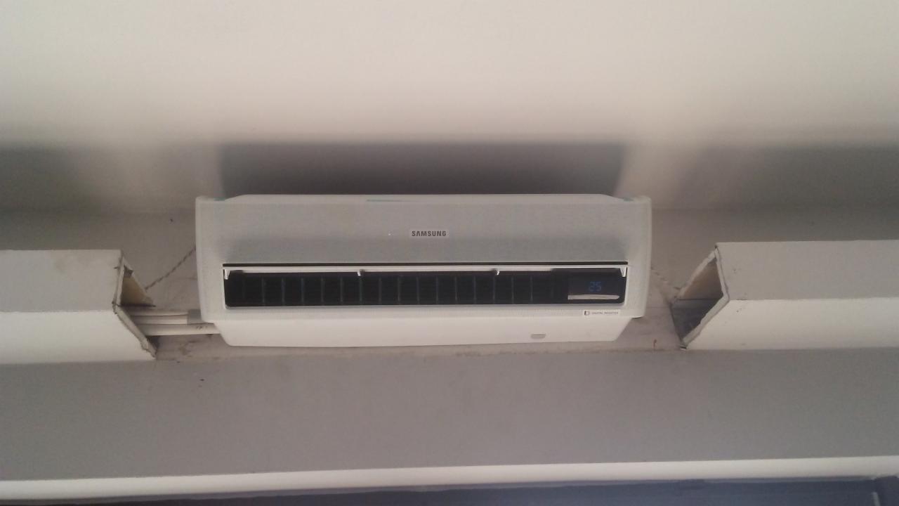 Biała klimatyzacja Samsung zamontowana pod sufitem, widoczne niedociągnięcia w obróbce wykończeniowej ścian.