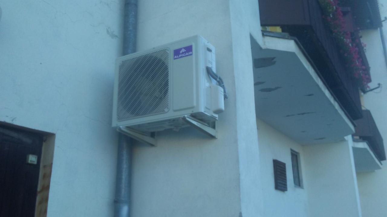 Zewnętrzna jednostka klimatyzacji Alpicair zamontowana na ścianie budynku, widok z dołu, obok rury spustowej.