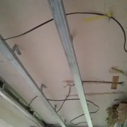 Widok na sufit z zamontowaną metalową konstrukcją pod płyty gipsowo-kartonowe, widoczne przewody elektryczne i fragment izolacji.