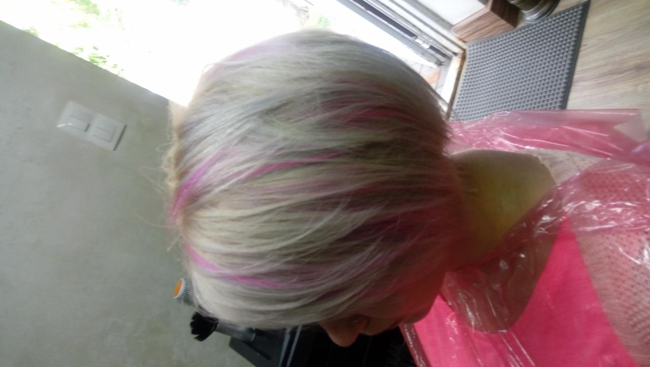 Blond włosy z różowymi pasemkami, widoczne z tyłu głowy, zabezpieczone różową peleryną fryzjerską.