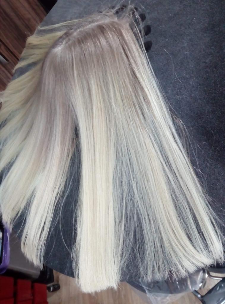 Blond pasma włosów z ciemniejszym odrostem, leżące na ciemnym tle, prawdopodobnie próbki koloryzacji.