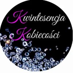 Okrągłe logo z napisem 'Kwintesencja Kobiecości' w kolorach różu i bieli na czarnym tle, ozdobione motywem rozsypanych diamentów.