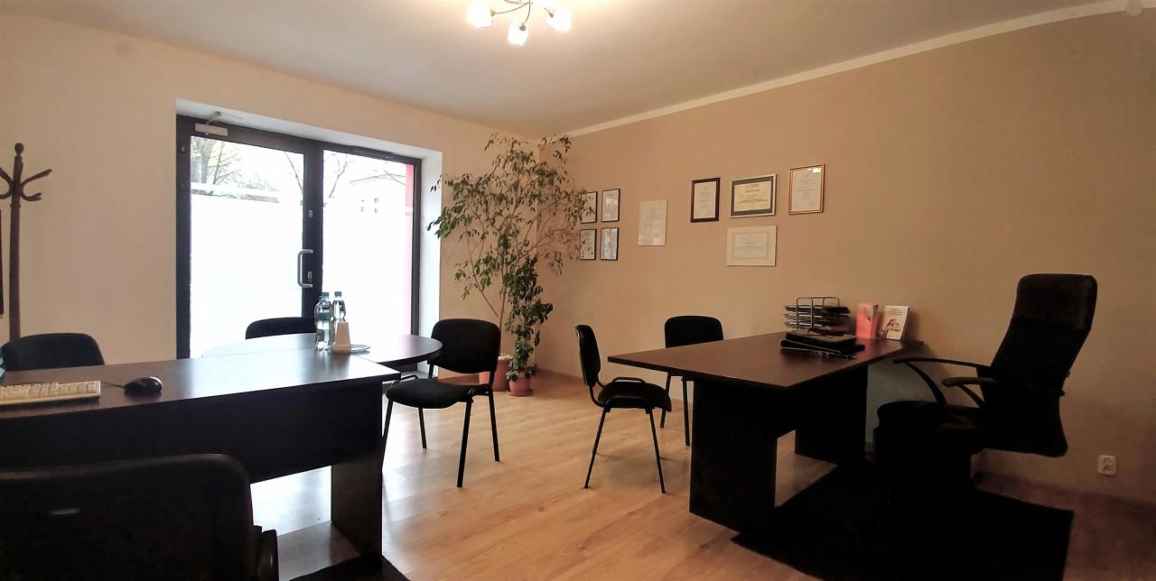 Jasne biuro nieruchomości w Dąbrowie Górniczej z biurkami, krzesłami i rośliną doniczkową, zdjęcia i certyfikaty na ścianie.