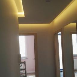 Marwoz - Korytarz w trakcie prac wykończeniowych z podwieszonym sufitem z oświetleniem LED, widoczna drabina, wiadro z farbą i zabezpieczona podłoga.