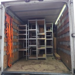 PL - Przeprowadzki Paweł Leonowicz - Wnętrze paki busa wypełnione metalowymi regałami i zabezpieczone pomarańczowymi pasami transportowymi, gotowe do przewozu. Widok z tyłu pojazdu.