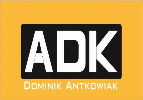 Logo firmy ADK Dominik Antkowiak na żółtym tle, czarna prostokątna tablica z białymi literami ADK i białym napisem 'Dominik Antkowiak' poniżej.