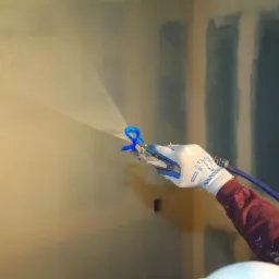 Praca z agregatem hydrodynamicznym podczas nakładania gładzi na ścianę, widoczne ślady po szpachlowaniu i niebieski przew&oacute;d doprowadzający materiał.