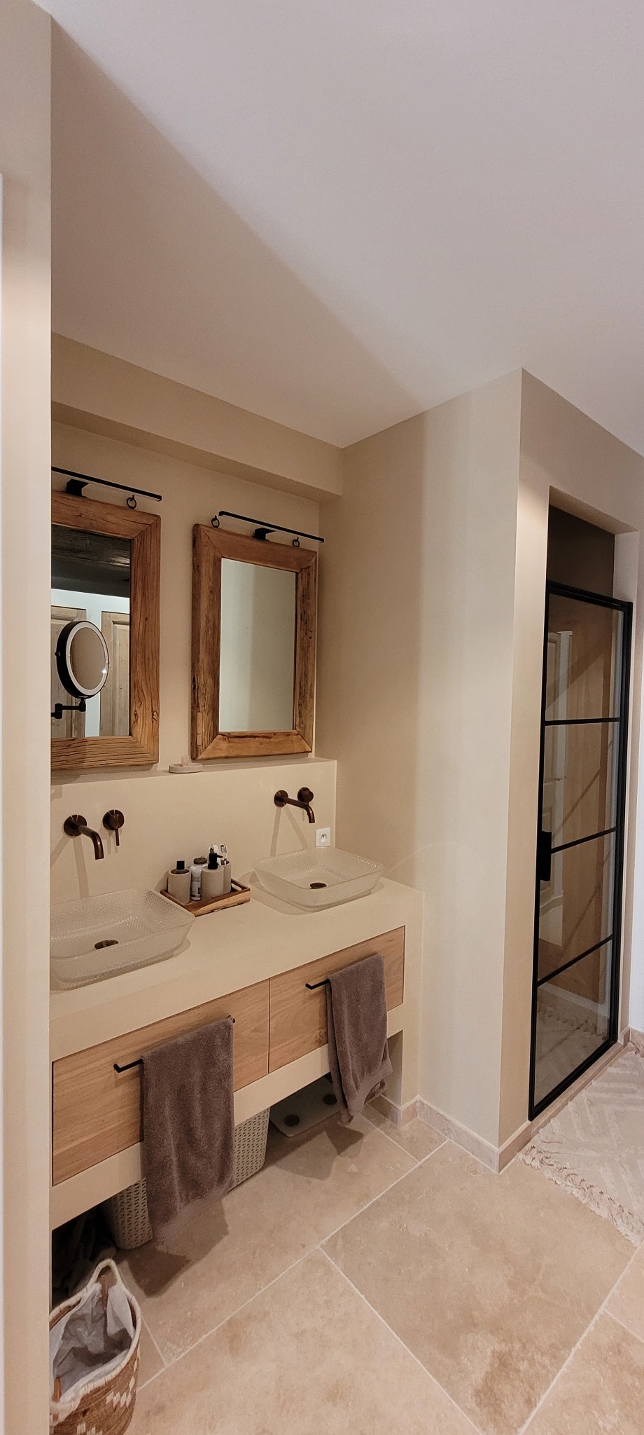 Beżowa łazienka z dwoma umywalkami o kwadratowym kształcie, drewnianymi ramami luster i kabiną prysznicową z czarnymi szprosami. Stonowana kolorystyka i naturalne materiały.