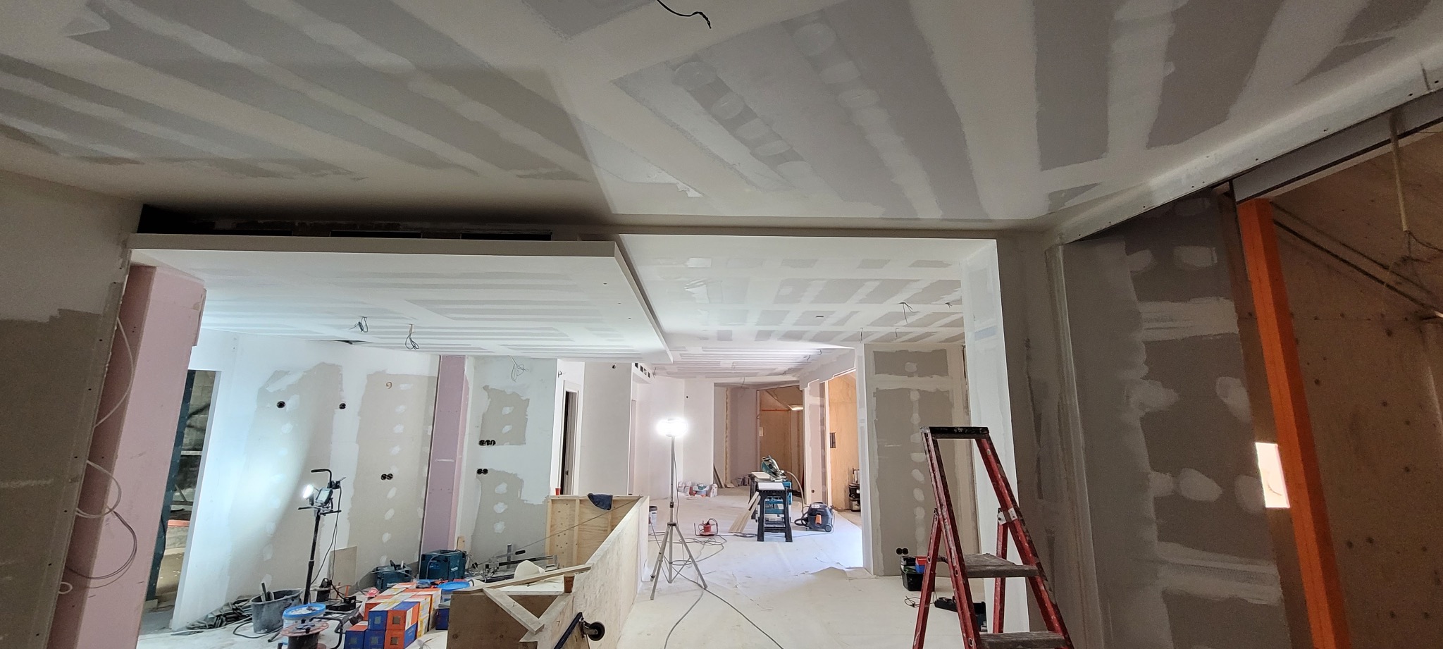 Wnętrze w trakcie prac wykończeniowych: sufit z płyt kartonowo-gipsowych z widocznymi łączeniami, ściany przygotowane do malowania, narzędzia i drabina w pomieszczeniu.