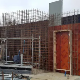 Zbrojenie fundamentów domu jednorodzinnego z widocznymi szalunkami i pracownikami na placu budowy.