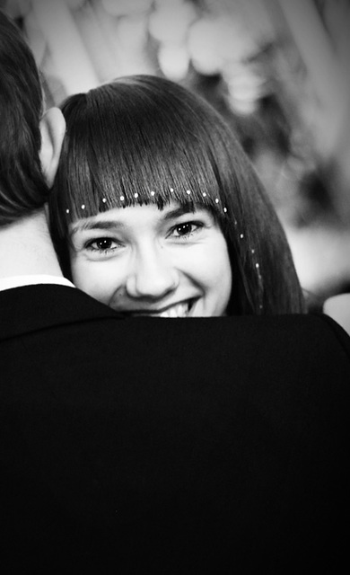 Czarno-białe zdjęcie uśmiechniętej kobiety z grzywką ozdobioną białymi kropkami, obejmującej mężczyznę w ciemnym garniturze.