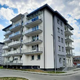 Nowoczesny budynek apartamentowy z balkonami z szklanymi balustradami, widok z poziomu ulicy w słoneczny dzień.