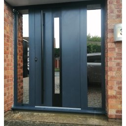 Inwest-Profil Spółka z Ograniczoną Odpowiedzialnością Spółka Komandytowa - Nowoczesne, przesuwne drzwi wejściowe w kolorze grafitowym z długim, pionowym uchwytem i wąskim przeszkleniem, zamontowane w budynku z cegły.