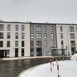 Inwest-Profil Spółka z Ograniczoną Odpowiedzialnością Spółka Komandytowa - Nowoczesny budynek mieszkalny z balkonami i szarymi żaluzjami w oknach, zimowy krajobraz.