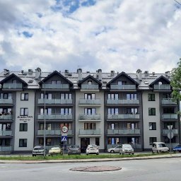 Inwest-Profil Spółka z Ograniczoną Odpowiedzialnością Spółka Komandytowa - Nowoczesny budynek wielorodzinny z szarymi oknami i balkonami z balustradami ze szkła, widok z poziomu ulicy w słoneczny dzień.