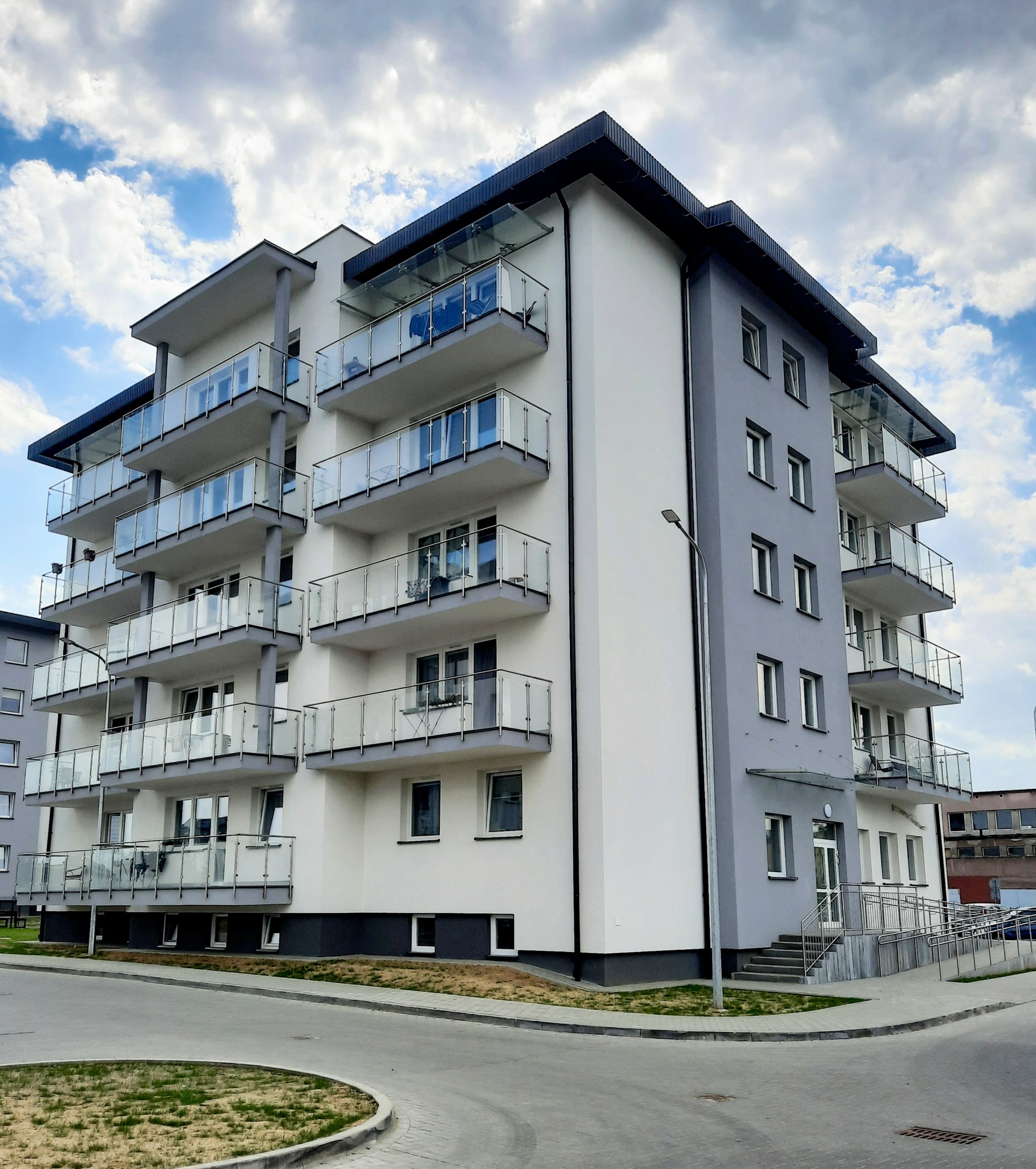 Nowoczesny budynek apartamentowy z balkonami z szklanymi balustradami, widok z poziomu ulicy w słoneczny dzień.