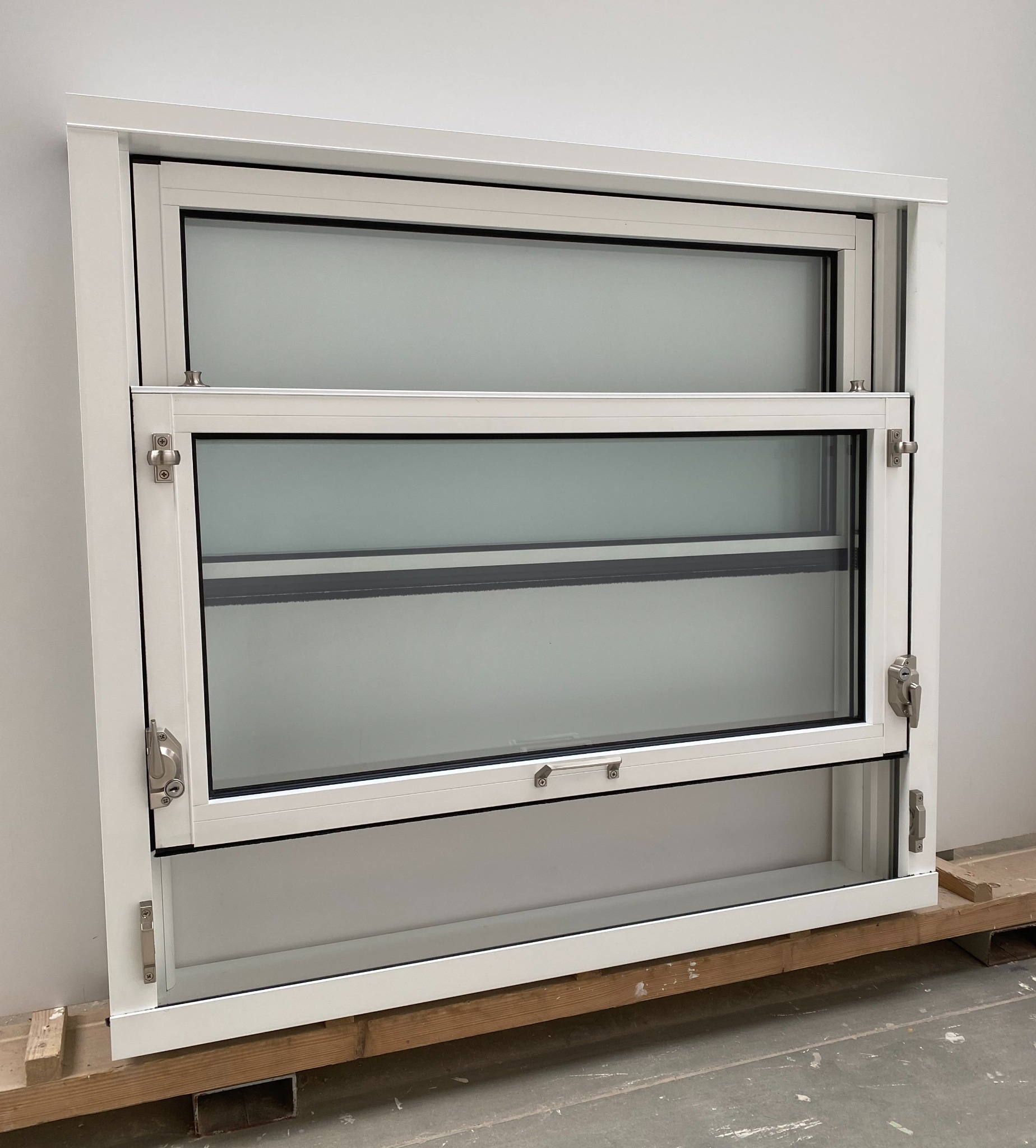 Białe, przesuwne okno z dwoma skrzydłami, widoczne detale okuć i mechanizmów przesuwnych, umieszczone na drewnianych paletach, gotowe do montażu.