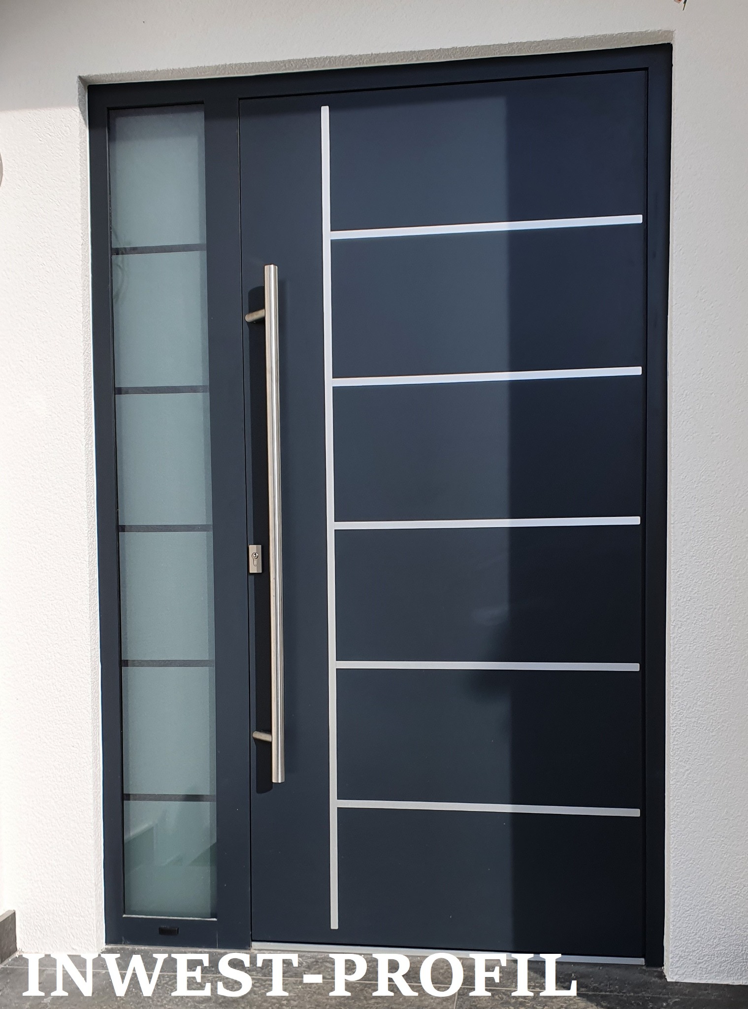 Nowoczesne, antracytowe drzwi wejściowe z przeszkleniem bocznym i długim, pionowym uchwytem, wkomponowane w białą elewację.