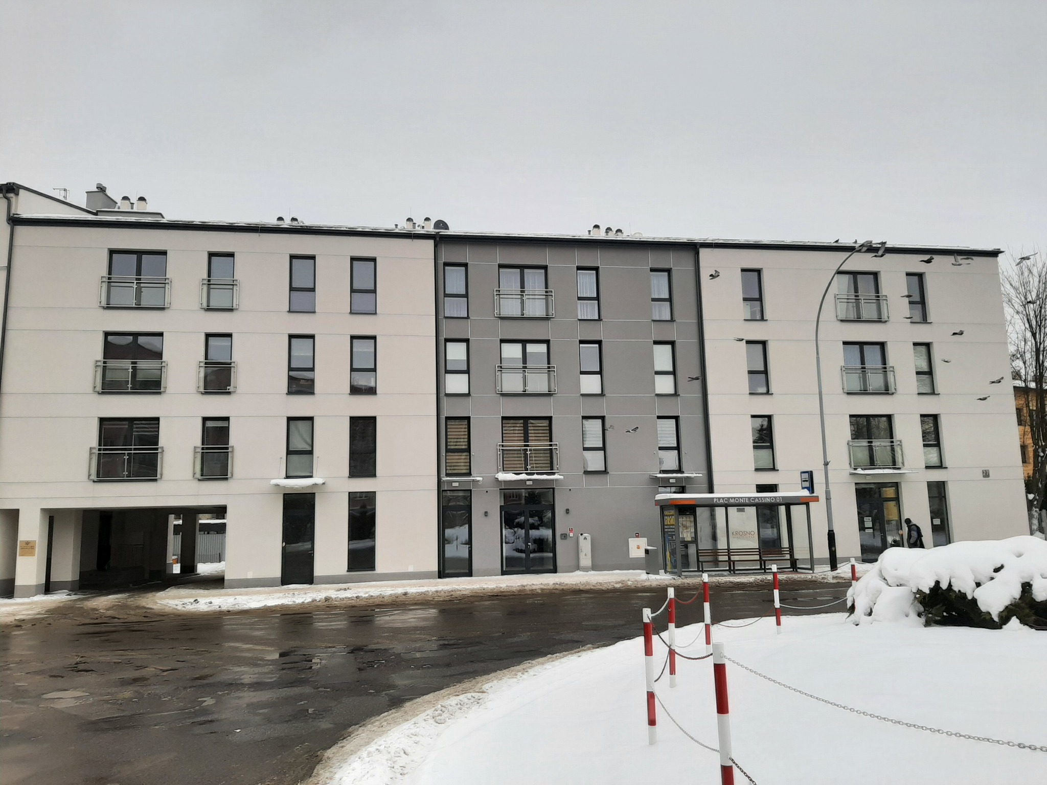 Nowoczesny budynek mieszkalny z balkonami i szarymi żaluzjami w oknach, zimowy krajobraz.