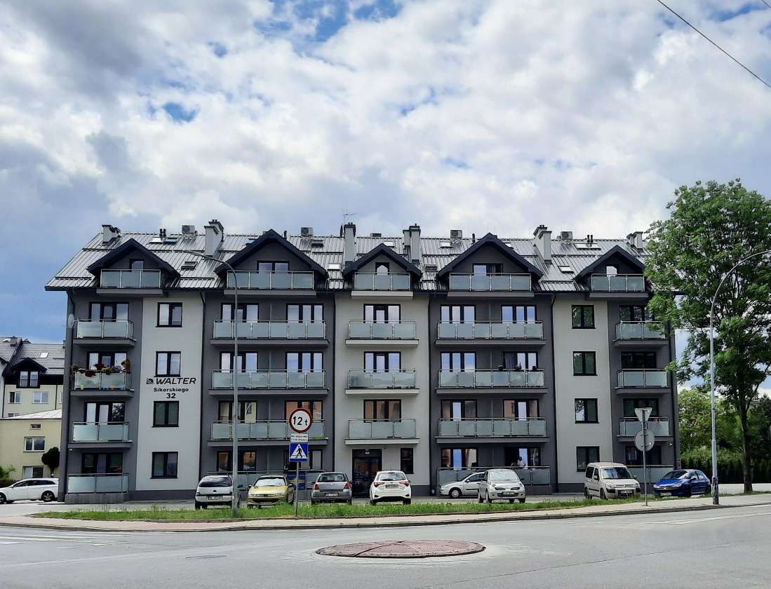 Nowoczesny budynek wielorodzinny z szarymi oknami i balkonami z balustradami ze szkła, widok z poziomu ulicy w słoneczny dzień.