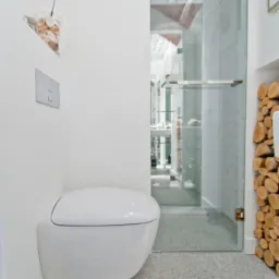 Nowoczesna łazienka z podwieszaną toaletą, szklaną kabiną prysznicową i dekoracyjnym drewnem kominkowym