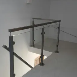 Szklana balustrada ze stalowymi słupkami i poręczą, widok z góry na schody w jasnym wnętrzu, podświetlona podłoga.