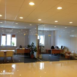 Zakład Ogólnobudowlany Bud-Dom Janusz Drzeszyński - Przeszklona ścianka działowa z drzwiami w biurze, widok na przestrzeń roboczą z biurkami i krzesłami, oświetlenie sufitowe.