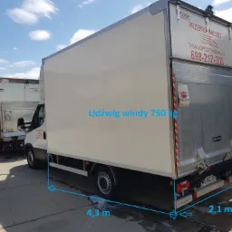 Dwa samochody dostawcze z windami załadowczymi, jeden z napisem 'Przeprowadzki Transportwawa24' i numerem telefonu, drugi w tle.