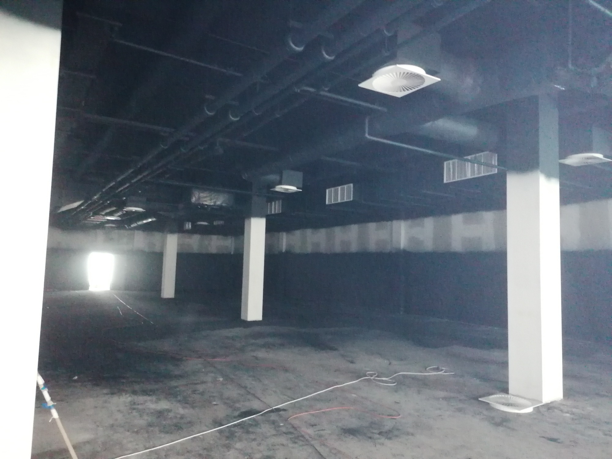 Wnętrze hali w trakcie prac instalacyjnych: widoczne rury pod sufitem, białe słupy i okablowanie na podłodze, przygotowane pod montaż systemów wentylacyjnych i klimatyzacyjnych.