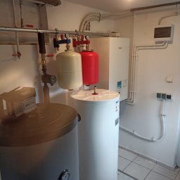WITVOLT SPÓŁKA Z OGRANICZONĄ ODPOWIEDZIALNOŚCIĄ - Bojlery w kotłowni: szary i biały, z instalacją hydrauliczną, manometrami i przewodami. Na ścianie biały piec grzewczy i instalacja elektryczna.