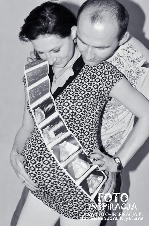 Czarno-białe zdjęcie przyszłych rodziców, kobieta w wzorzystej sukience trzyma na brzuchu pasek zdjęć USG, mężczyzna obejmuje ją czule.