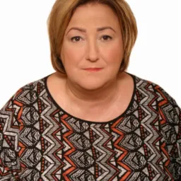 Portret kobiety o blond włosach w bluzce z geometrycznym wzorem na białym tle, skierowanej wprost, z lekkim uśmiechem.