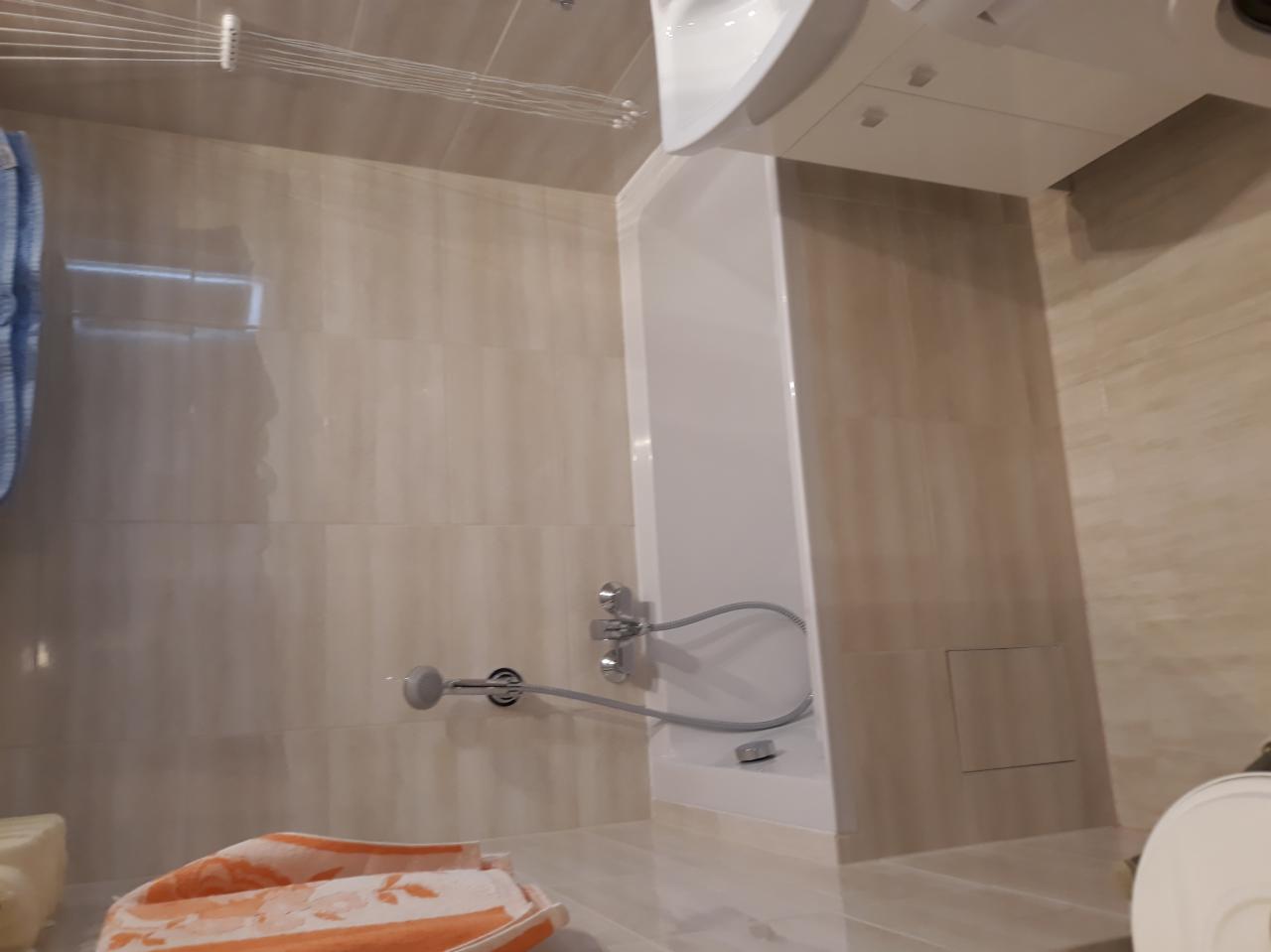 Wykończona łazienka z beżowymi, połyskującymi płytkami, kabiną prysznicową z baterią natryskową i suszarką na pranie pod sufitem.