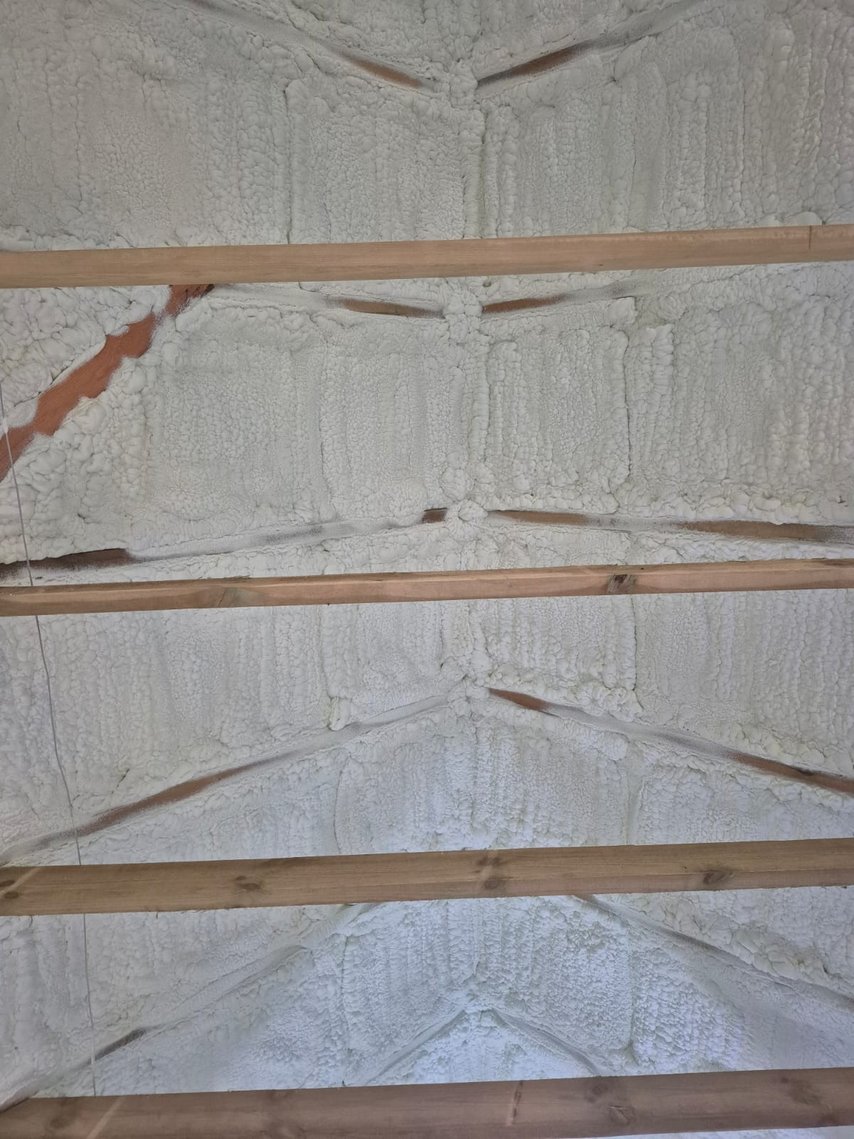 Ocieplenie poddasza pianką natryskową, widoczne drewniane belki konstrukcyjne. Aplikacja piany w trudno dostępnych miejscach, równomierna warstwa izolacji.