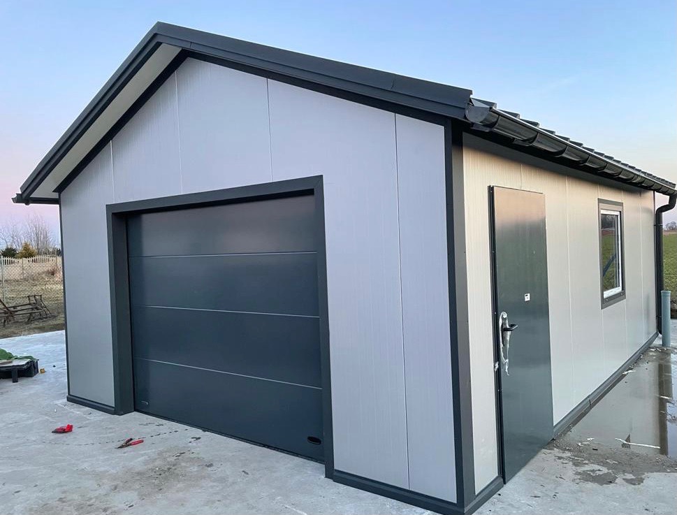 Gotowy garaż z płyt warstwowych w kolorze szarym, z bramą segmentową i drzwiami wejściowymi, widoczne narzędzia na posadzce.