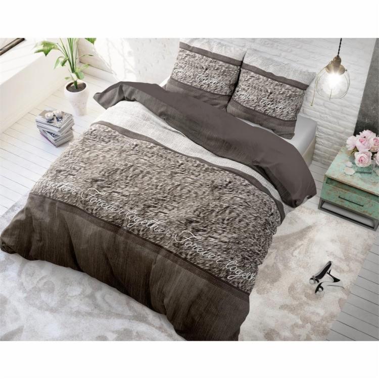 Brązowo-szara pościel z napisem 'Forever Together' na łóżku w jasnym pokoju z ceglaną ścianą, obok stolik nocny z różowymi kwiatami i lampa wisząca.