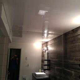 Sufity napinane Grudziądz - Błyszczący, kremowy sufit napinany w łazience z ciemną, drewnopodobną ścianą i odbiciem fotografa.