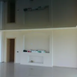 Błyszczący, czarny sufit napinany w jasnym salonie z dużym oknem i wnęką w ścianie, widoczne lampki ścienne.