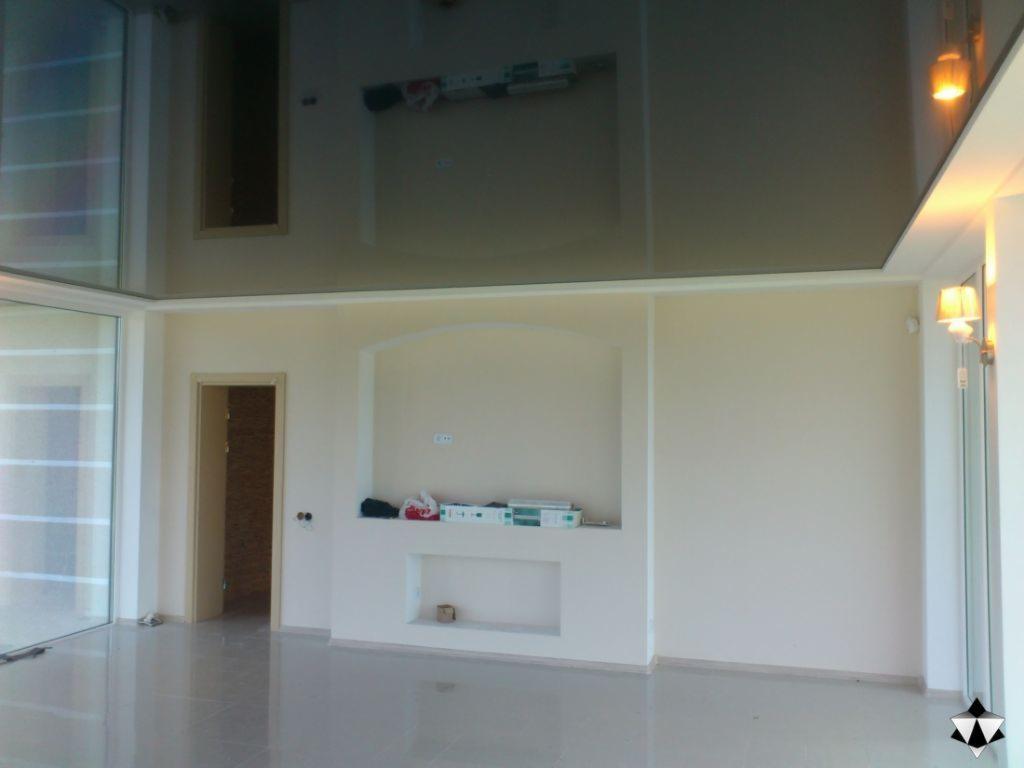 Błyszczący, czarny sufit napinany w jasnym salonie z dużym oknem i wnęką w ścianie, widoczne lampki ścienne.