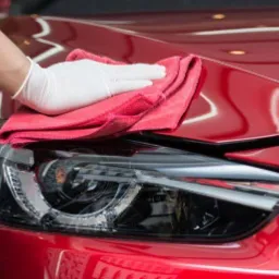 Ręka w białej rękawiczce poleruje czerwoną karoserię samochodu za pomocą czerwonej mikrofibry, reflektor w zbliżeniu.