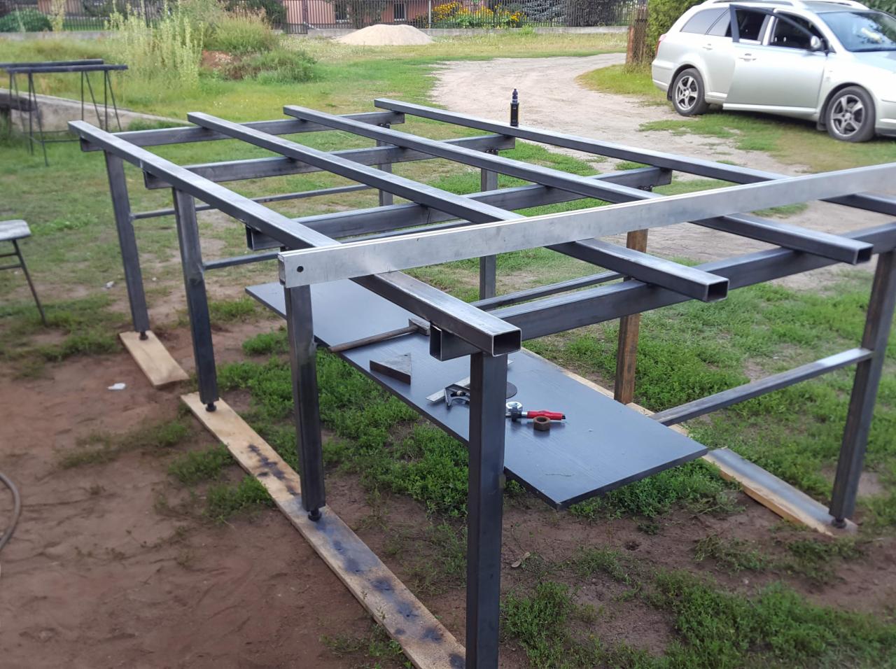 Konstrukcja szkieletowa z metalowych profili w trakcie budowy w miejscowości Blochy, widoczne narzędzia i elementy mocujące na blacie roboczym.