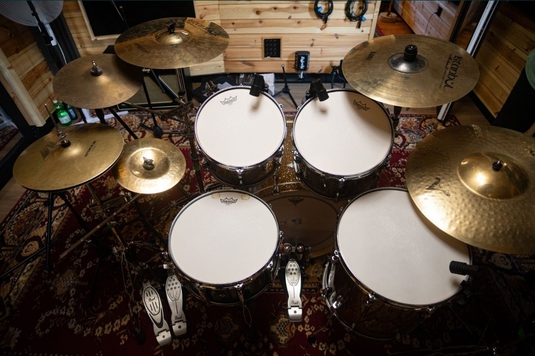 Zestaw perkusyjny z mikrofonami w studiu nagraniowym, widok z góry, dywan z orientalnym wzorem, drewniane ściany.
