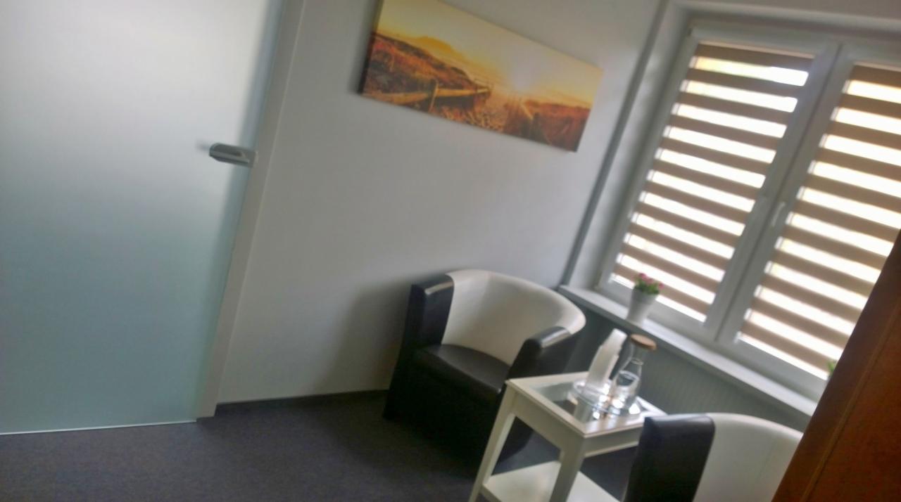 Nowoczesne wnętrze biura z dwoma fotelami, stolikiem z wodą i obrazem krajobrazu nad oknem z żaluzjami.