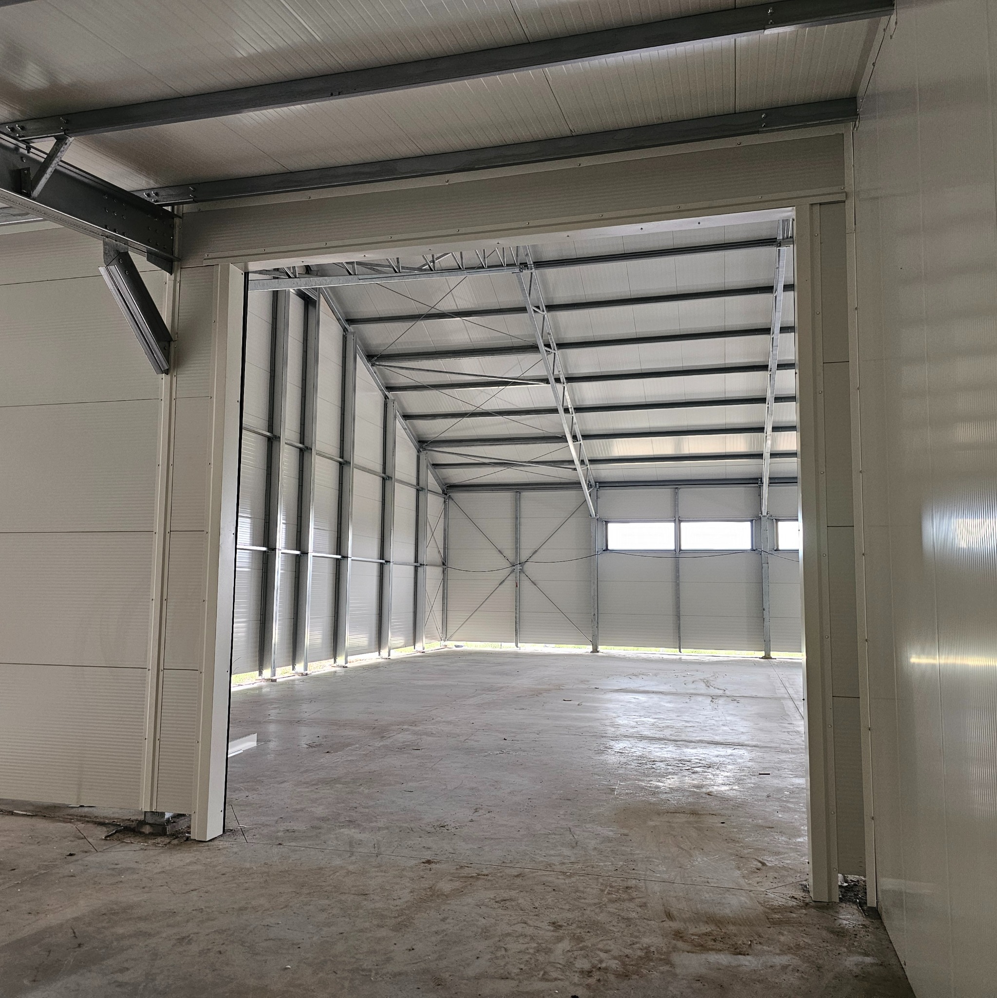 Wnętrze nowo wybudowanej, pustej hali z widoczną stalową konstrukcją nośną i panelami ściennymi, sfotografowane z poziomu wejścia.